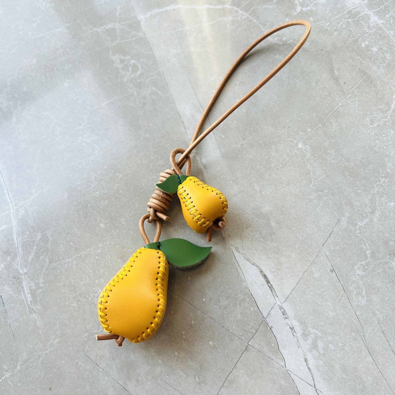 May include: A yellow leather keychain with two pear charms. The pears are stitched with brown thread and have green leaves.