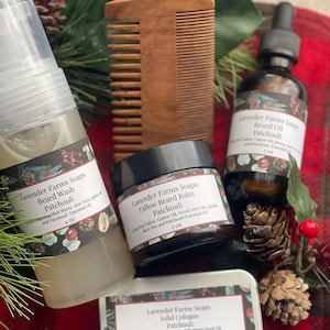 May include: A collection of beard care products, including beard wash, beard oil, beard balm, and solid cologne, with a wooden comb. The products are labeled "Lavender Farms Soaps Patchouli" and are arranged on a red and black plaid surface.