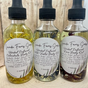 May include: Three glass bottles of herbal infused body oil. The bottles are labeled "Lavender Farms Soaps" and each bottle has a different flower inside: calendula, wild violet, and rose. Each bottle is 2 ounces.