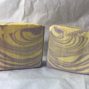 May include: Two bars of handmade soap with a swirl pattern in shades of yellow and purple.
