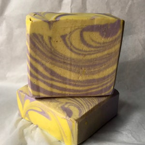 May include: Two bars of handmade soap with a swirl pattern in shades of yellow and purple.