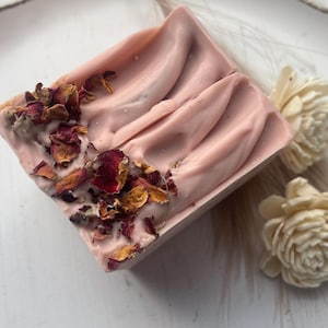 May include: A pink soap bar with dried rose petals embedded in the surface. The soap has a smooth, slightly textured surface.