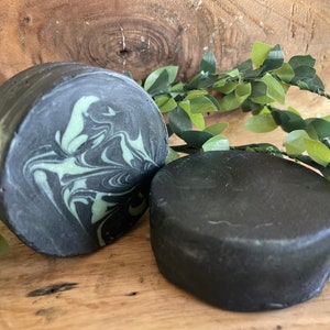 Puede incluir: Dos barras redondas de jab&oacute;n negro y verde. Una barra tiene un patr&oacute;n de remolino de verde y negro, mientras que la otra barra es de color negro s&oacute;lido.