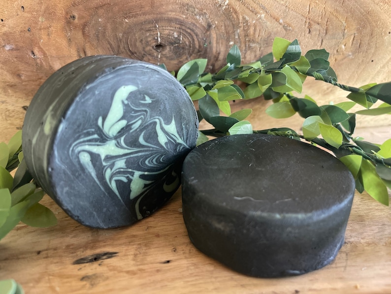 Puede incluir: Dos barras redondas de jab&oacute;n negro y verde. Una barra tiene un patr&oacute;n de remolino de verde y negro, mientras que la otra barra es de color negro s&oacute;lido.