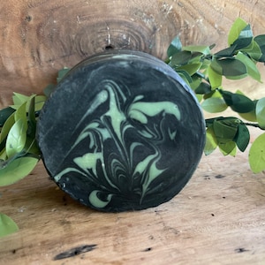 May include: A round, black and green soap bar with a marbled design.