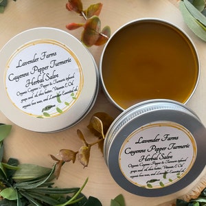 May include: Two silver tins of cayenne pepper turmeric herbal salve. The label on the tin reads "Lavender Farms Cayenne Pepper Turmeric Herbal Salve. Organic Cayenne Pepper & Turmeric infused grape seed oil, shea butter, Vitamin E oil, organic bees wax, and Lavender Essential oil."