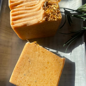 May include: Two bars of handmade soap, one with dried flowers on top, both with a light orange color.