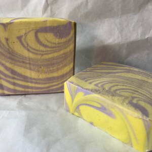 May include: Two bars of handmade soap with a swirl pattern in shades of yellow and purple.