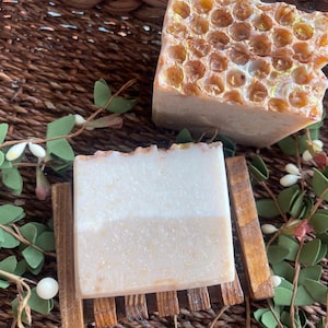 May include: Two bars of handmade soap, one with a honeycomb design and the other with a white and beige swirl. The soap bars are on a wooden soap dish.