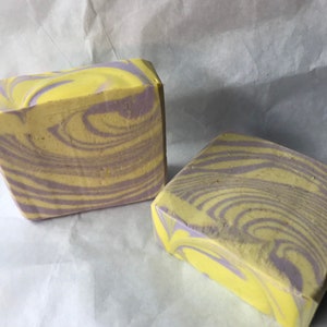 May include: Two bars of handmade soap with a swirl pattern of yellow and purple.