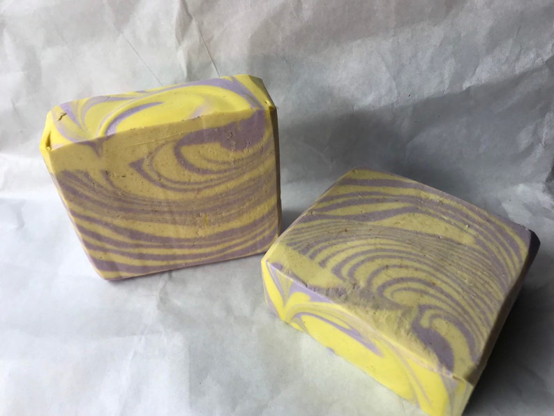 May include: Two bars of handmade soap with a swirl pattern of yellow and purple.