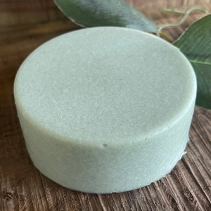 May include: A round, light blue bar of soap. The soap is on a wooden surface.