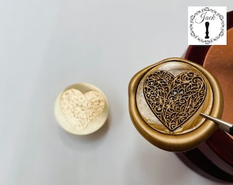 May include: A gold heart-shaped wax seal with a detailed floral design. The seal is on a wooden surface.