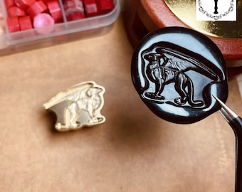 Könnte beinhalten: Ein schwarzes Wachssiegel mit einem detaillierten Bild eines Greifs, einer mythischen Kreatur mit dem Kopf und den Flügeln eines Adlers und dem Körper eines Löwen. Das Siegel wird von einer Pinzette gehalten.