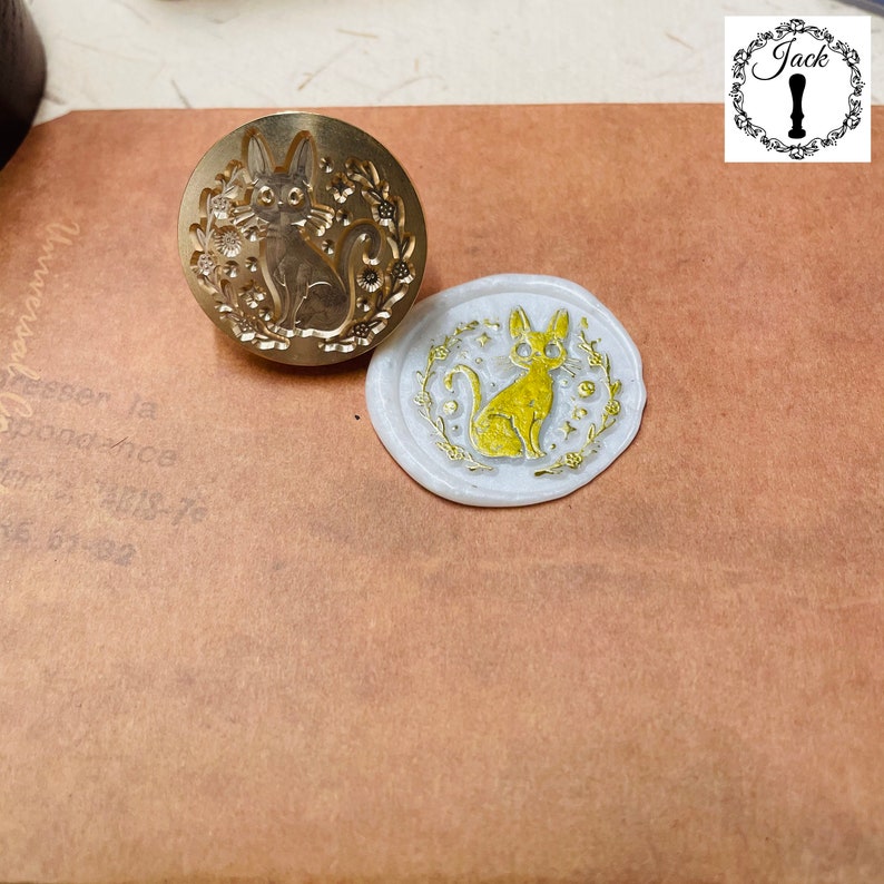 May include: Two wax seals featuring a gold cat design. The seal on the left is a brass stamp, and the seal on the right is a wax impression.