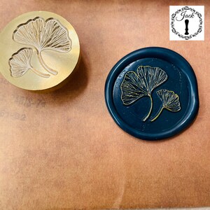 May include: A gold metal stamp with a design of two ginkgo leaves. A blue wax seal with a gold ginkgo leaf design.