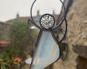 May include: A stained glass angel ornament with a white opalescent body and a clear glass halo. The angel is hanging from a window.