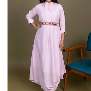 May include: A pink long-sleeved dress with a collared neckline and a decorative belt. The dress has a flowing skirt and is worn by a person with long dark hair.