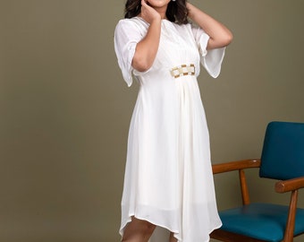 May include: A white dress with a gold belt and a high-low hemline. The dress is made of a lightweight fabric and has a relaxed fit. The model is wearing the dress with nude heels.