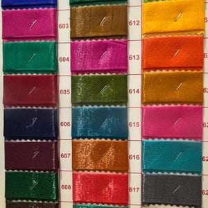 May include: A color swatch card featuring samples of fabric in various colors, including red, blue, pink, green, and brown. Each sample is rectangular and pinned to the card, with numbers indicating the color code.