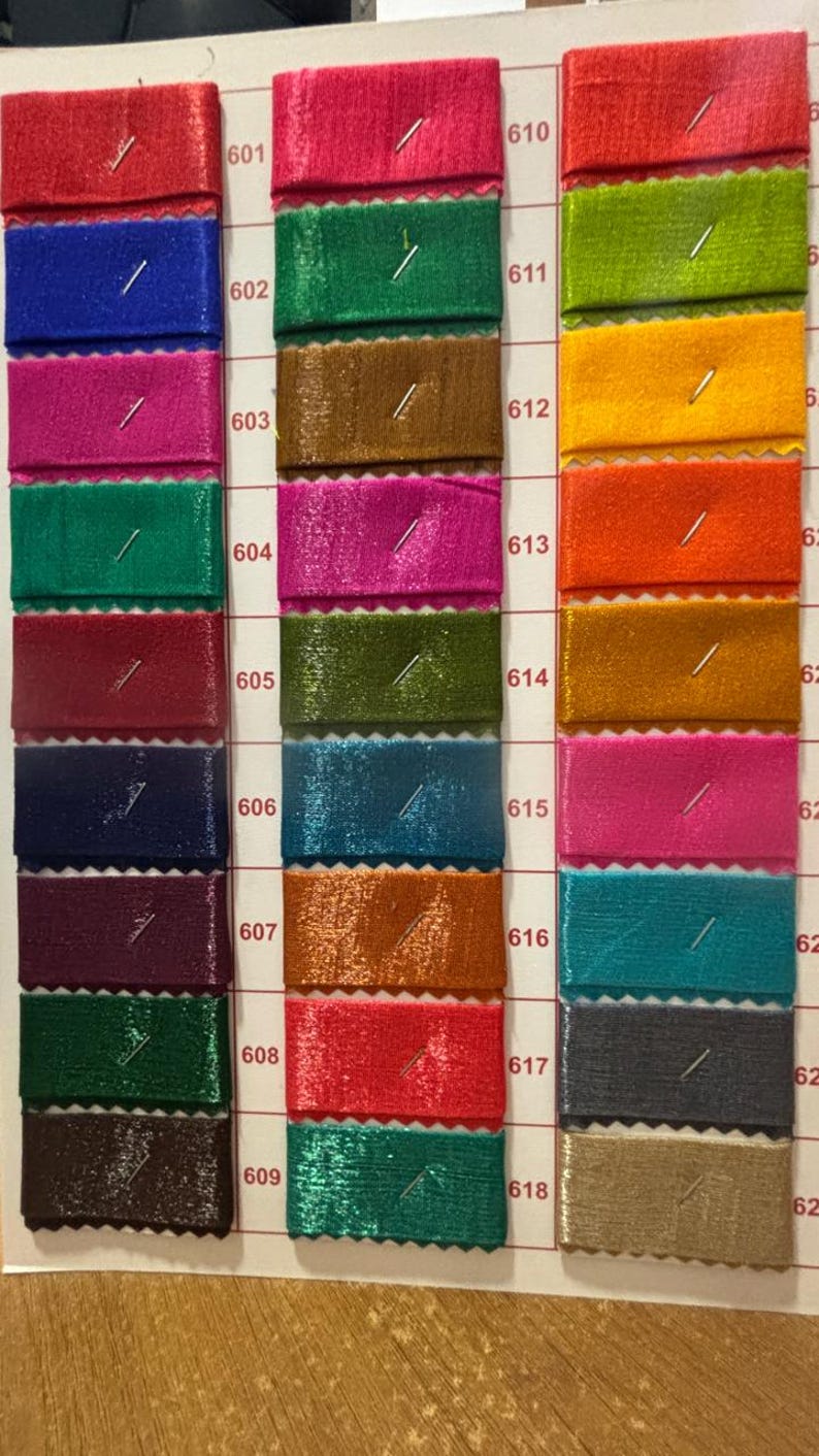 May include: A color swatch card featuring samples of fabric in various colors, including red, blue, pink, green, and brown. Each sample is rectangular and pinned to the card, with numbers indicating the color code.