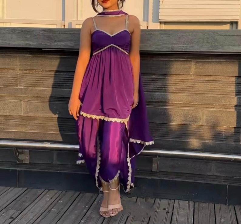 Puede incluir: Un vestido morado con escote de coraz&oacute;n y ribete de encaje. El vestido tiene una falda fluida y se combina con pantalones morados a juego.