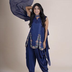 May include: A woman wearing a navy blue salwar kameez with floral embroidery. The kameez has a long, flowing sleeve and the salwar is a loose, comfortable style.
