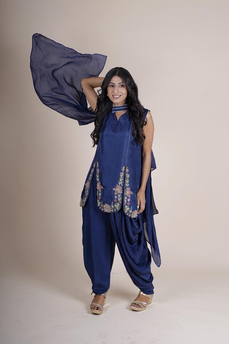 May include: A woman wearing a navy blue salwar kameez with floral embroidery. The kameez has a long, flowing sleeve and the salwar is a loose, comfortable style.