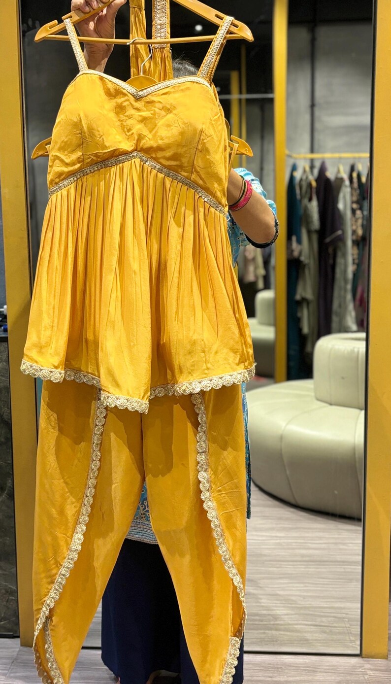 Puede incluir: Un conjunto de dos piezas de color amarillo mostaza con una blusa sin mangas y pantalones. La blusa tiene un escote de coraz&oacute;n y un dobladillo con volantes. Los pantalones tienen una pierna ancha y un ribete de encaje.