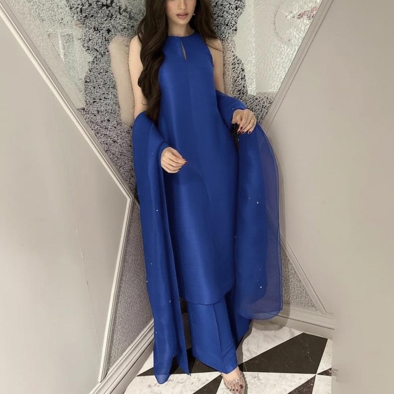 May include: A vibrant blue ensemble featuring a sleeveless top with a keyhole detail and matching wide-leg pants. A sheer scarf with subtle embellishments drapes over the shoulders. The outfit is made of a smooth, flowing fabric.
