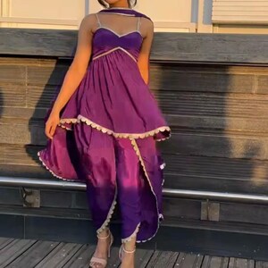 Puede incluir: Un vestido morado de capas con un dobladillo con volantes y ribetes dorados. El vestido tiene un escote de coraz&oacute;n y se lleva con un dupatta morado a juego.