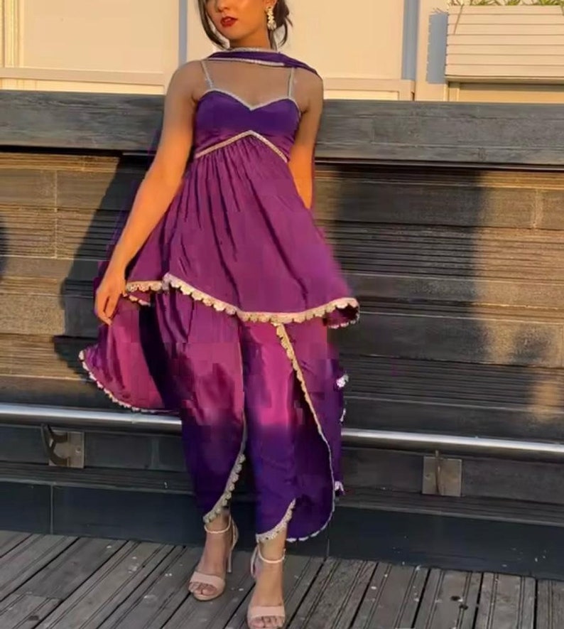 Puede incluir: Un vestido morado de capas con un dobladillo con volantes y ribetes dorados. El vestido tiene un escote de coraz&oacute;n y se lleva con un dupatta morado a juego.