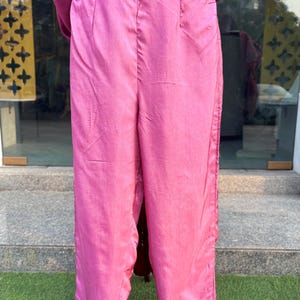 May include: Pink wide-leg pants with a satin finish. The pants have a high waist and a straight leg.