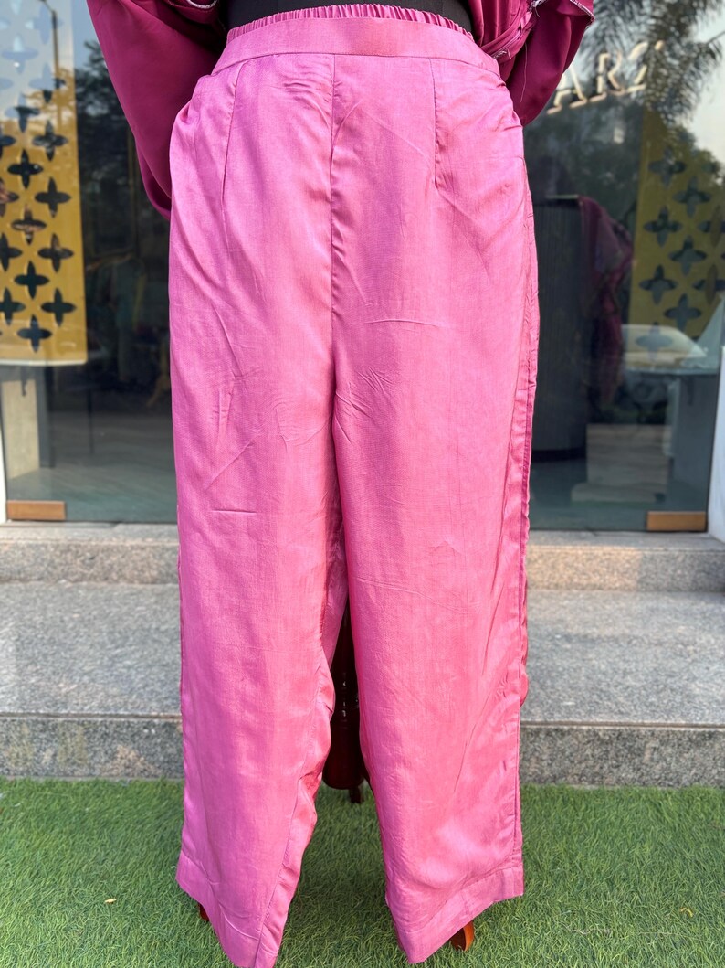 May include: Pink wide-leg pants with a satin finish. The pants have a high waist and a straight leg.