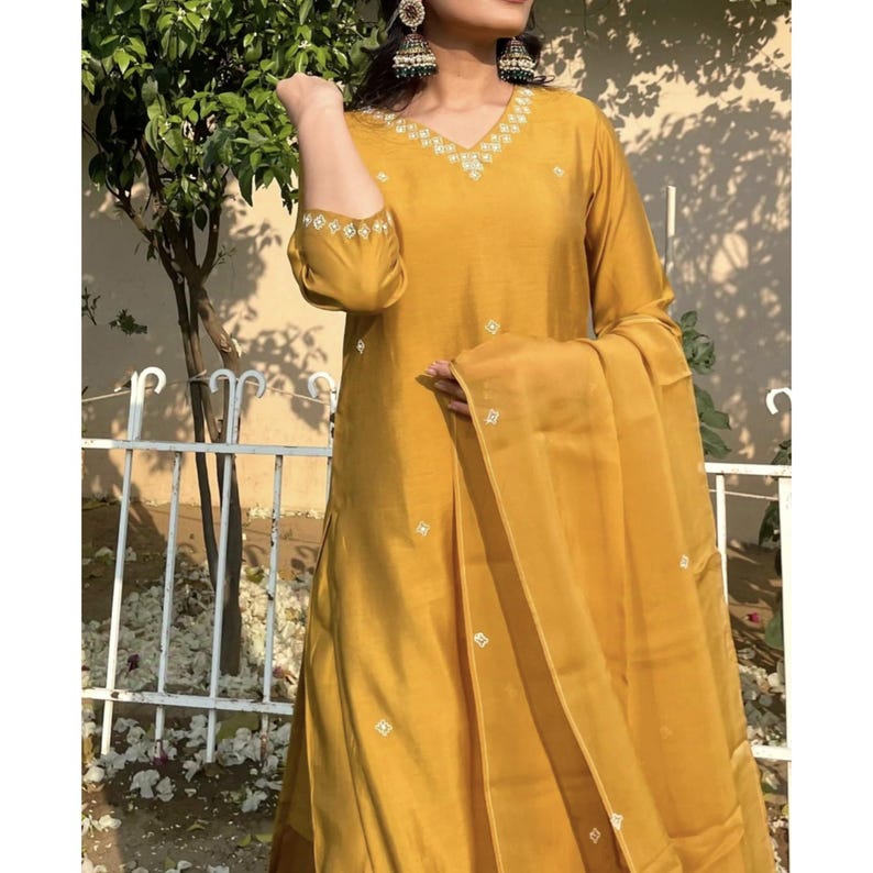May include: A mustard yellow embroidered kurta with a matching dupatta. The kurta has a V-neckline and three-quarter sleeves. The dupatta is sheer and has a delicate embroidered border.