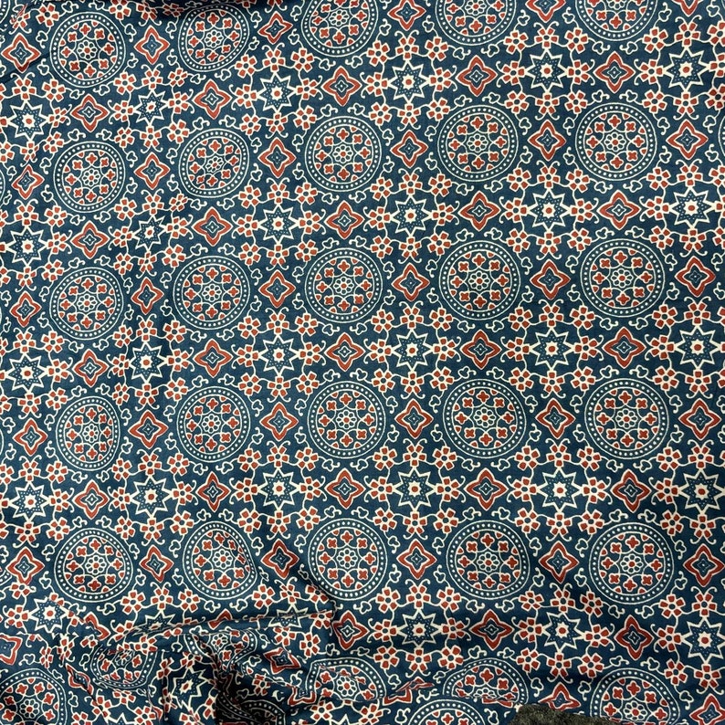 Op de afbeelding: Een blauwe stof met een herhalend patroon van rode en witte cirkels en sterren. De stof heeft een traditioneel Indiaas ontwerp.