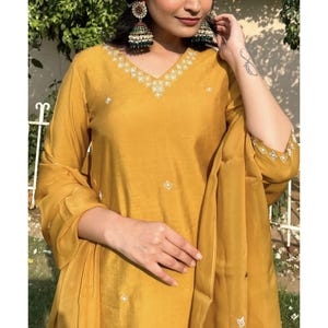 May include: A mustard yellow kurta with a V-neckline and intricate white embroidery. The kurta has long sleeves and is paired with a matching dupatta.