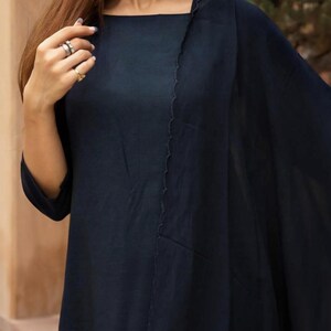May include: A navy blue long-sleeved tunic with a high neckline and a single, angled seam on the front. The tunic is made of a lightweight fabric and has a flowing silhouette.