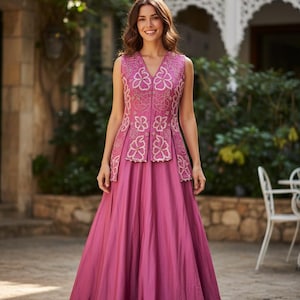 Puede incluir: Vestido de fiesta magenta sin mangas con escote en V. El corpiño presenta intrincados bordados florales en un tono más claro, y la falda llega hasta el suelo. Adecuado para ocasiones especiales.