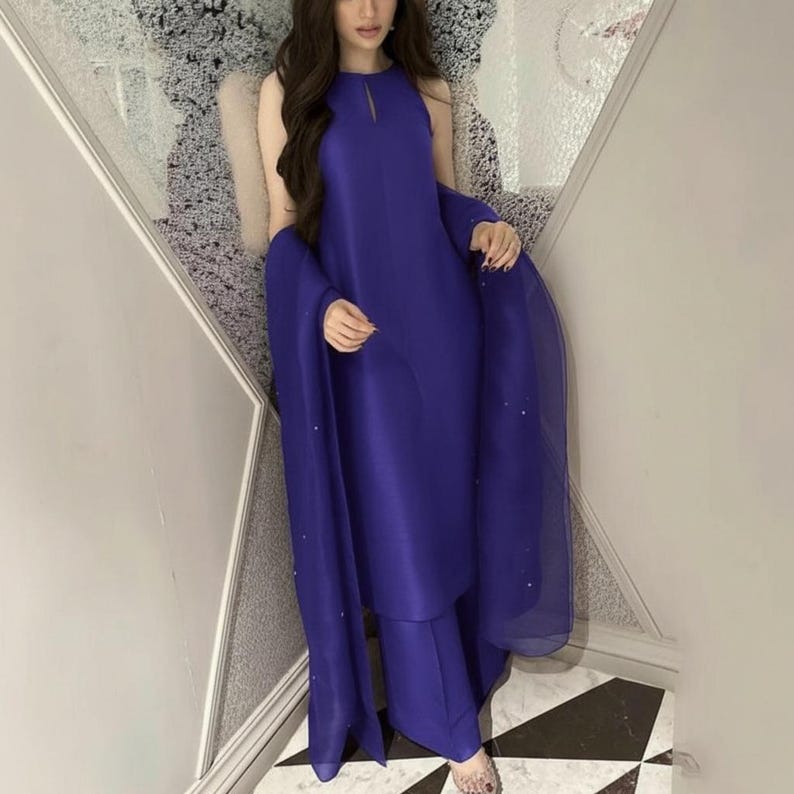 May include: A vibrant blue formal outfit, featuring a sleeveless top with a keyhole detail, matching wide-leg pants, and a sheer scarf. The outfit is made of a smooth, flowing fabric. The ensemble is suitable for special occasions.