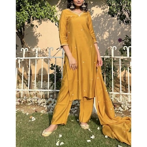 May include: A mustard yellow kurta set with white embroidery. The set includes a long-sleeved kurta, matching pants, and a dupatta.