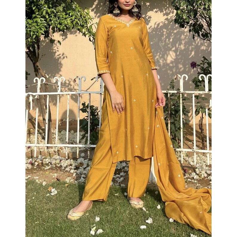 May include: A mustard yellow kurta set with white embroidery. The set includes a long-sleeved kurta, matching pants, and a dupatta.