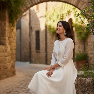 Seated side view showing drape of lightweight muslin, three-quarter sleeves and palazzo, white anarkali suit