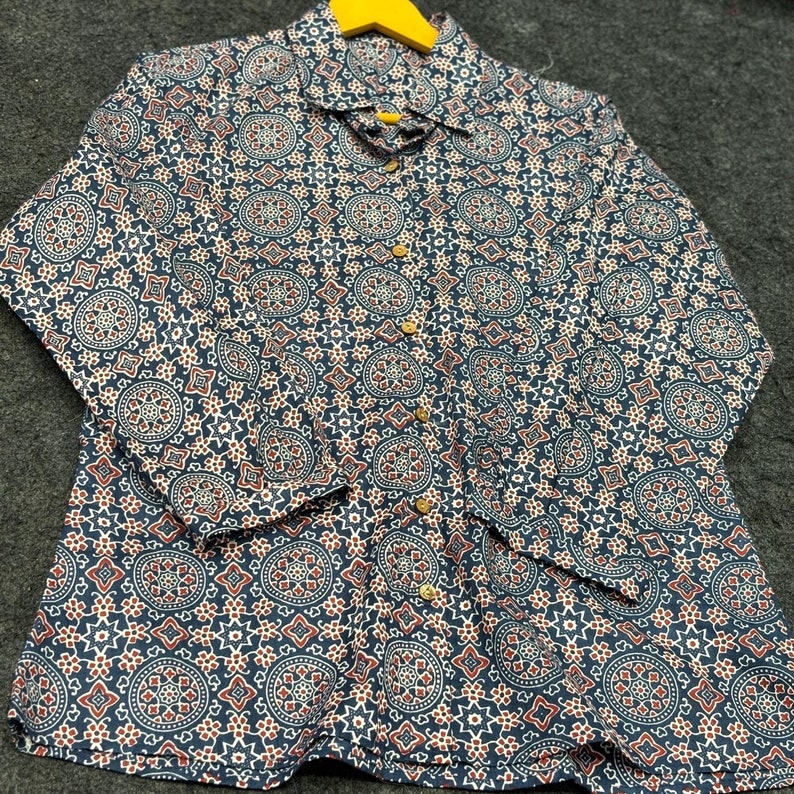 Op de afbeelding: Een lang mouw shirt met een blauw en wit patroon. Het patroon heeft ingewikkelde geometrische vormen en een rode accentkleur.