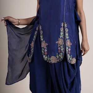 A blue sleeveless top with floral embroidery and a matching blue dhoti pant. The top has a keyhole neckline and a slit on the front. The dhoti pant has a loose fit and is gathered at the waist.