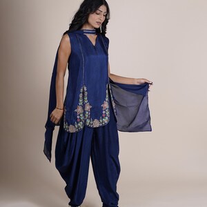 May include: A woman wearing a navy blue salwar kameez with floral embroidery. The outfit includes a long, sleeveless top with a V-neckline and a pair of matching pants.