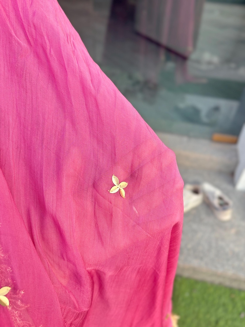 May include: A close-up of a pink fabric with gold embellishments in the shape of flowers. The fabric is sheer and has a delicate texture.