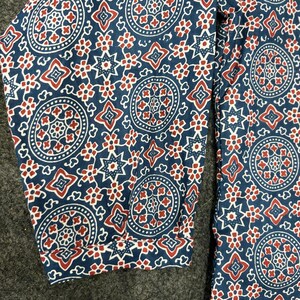 Op de afbeelding: Blauwe stof met een rood en wit geometrisch patroon. Het patroon bevat cirkels, sterren en vierkanten.