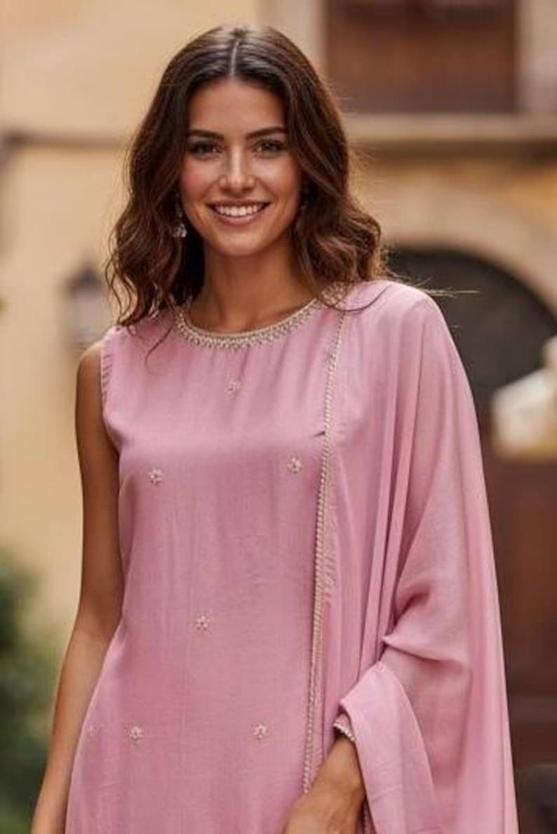May include: A sleeveless, dusty rose-colored outfit with delicate floral embroidery. The ensemble includes a top with a beaded neckline and a matching draped shawl. The outfit is made of a soft, flowing fabric, perfect for a special occasion.