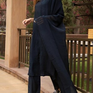 May include: A woman wearing a navy blue three-piece outfit, including a long-sleeved top, pants, and a sheer dupatta. The outfit is made of a soft, flowing fabric. The woman is standing on a stone path.